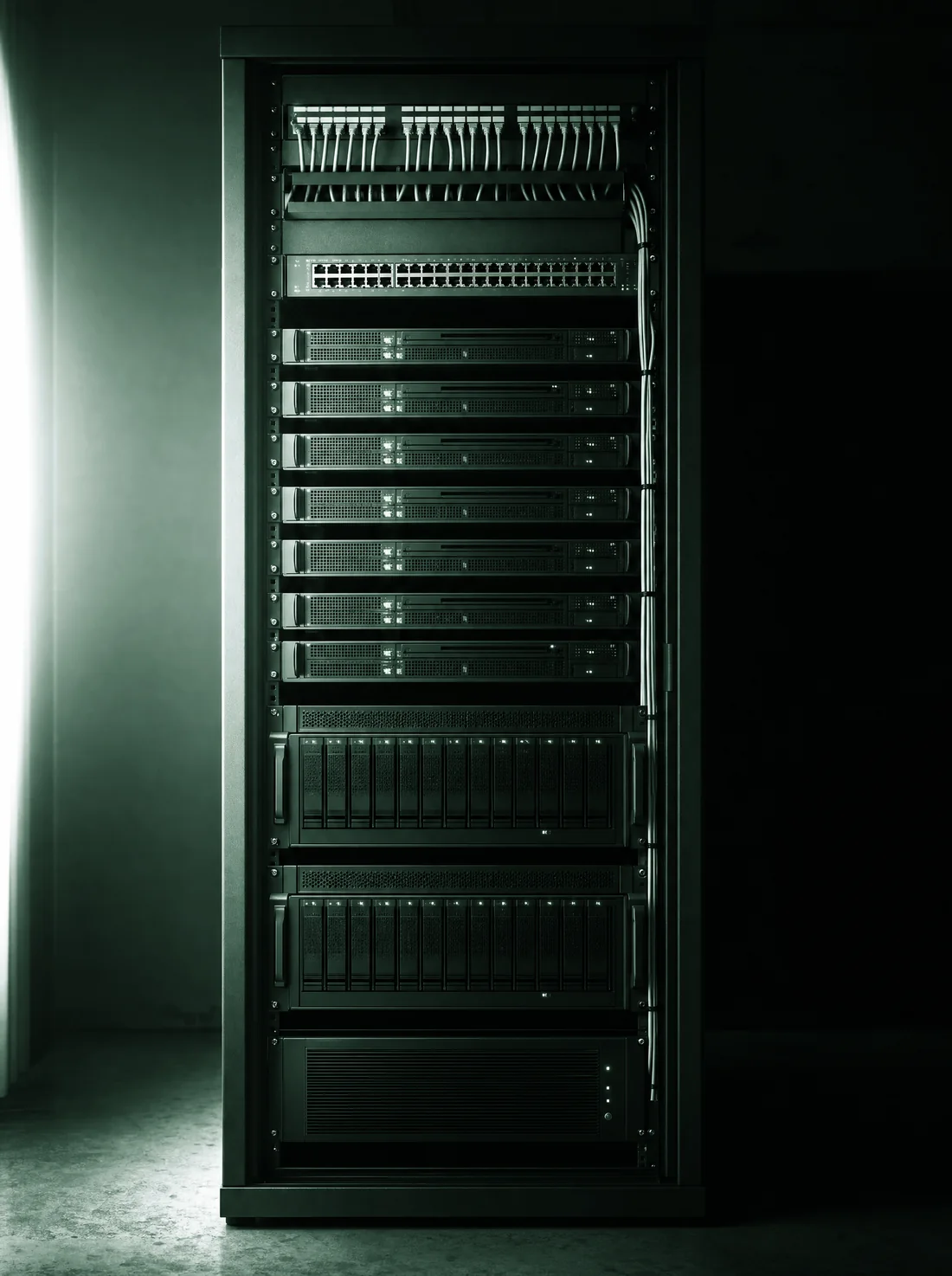 A fully populated 42U enterprise rack photographed square-on in a dark room: cable management and a patch panel at the top, a switch, a stack of thin compute nodes, two large drive chassis, and a power unit at the base.